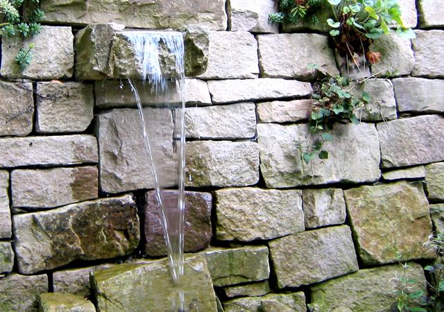 Natursteinmauer mit kleinem Wasserspeier.